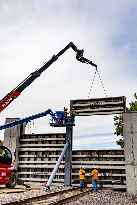 Large crane placing horizontal sections of metal into vertical slats within concrete retaining wall