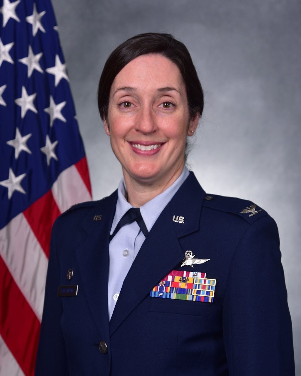 Woman in dress blues posing for official photo in front of U.S. flag