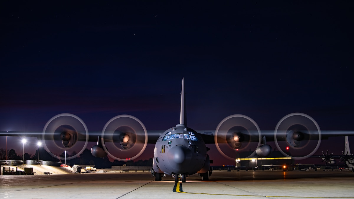 A military cargo aircraft on the parking ramp with the propeller blades spinning.