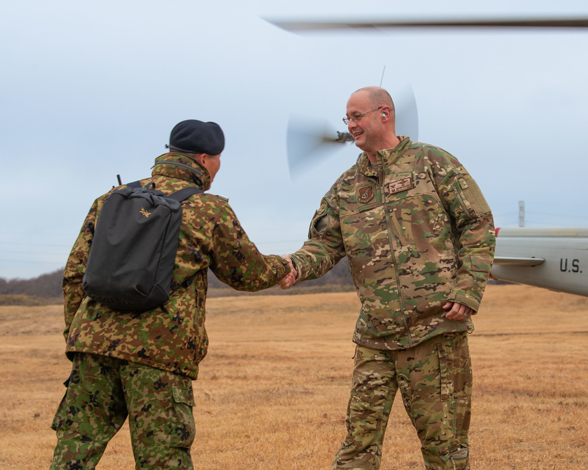 Two men shake hands in front of a helicopter