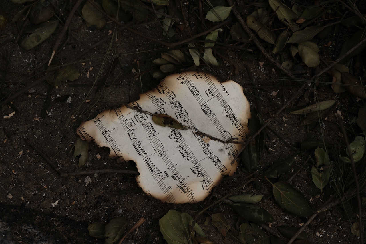 A mostly charred sheet of music lies on the ground on dirt.