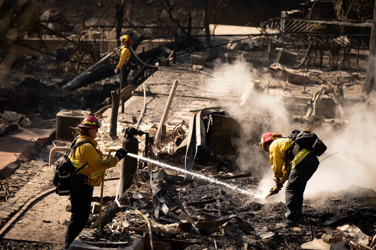 Three firefighters hose down the remains of a building burned down by a wildfire.