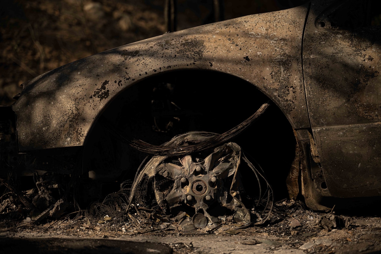 A charred, ruined front of a vehicle and wheel is shown during low-light conditions.
