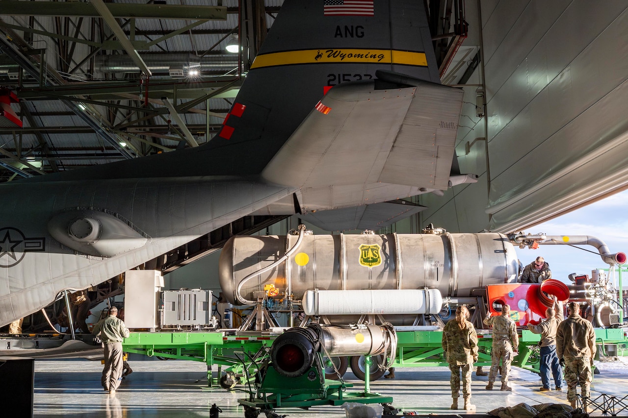 A group of airmen load large firefighting equipment onto the ack of a large aircraft cargo bay while inside a hangar.