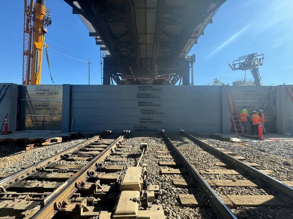 A temporary barrier being erected over two rail tracks underneath bridge