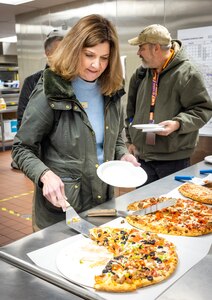 Julia McLaughlin, director, Morale Welfare and Recreation, Naval Base Kitsap-Bremerton, dishes up a slice of freshly baked pizza from the Picnic Pizza Station, a new automated pizza oven, Dec. 9, 2024, inside the Building 435 cafeteria at Puget Sound Naval Shipyard & Intermediate Maintenance Facility in Bremerton, Washington. (U.S. Navy photo by Wendy Hallmark)