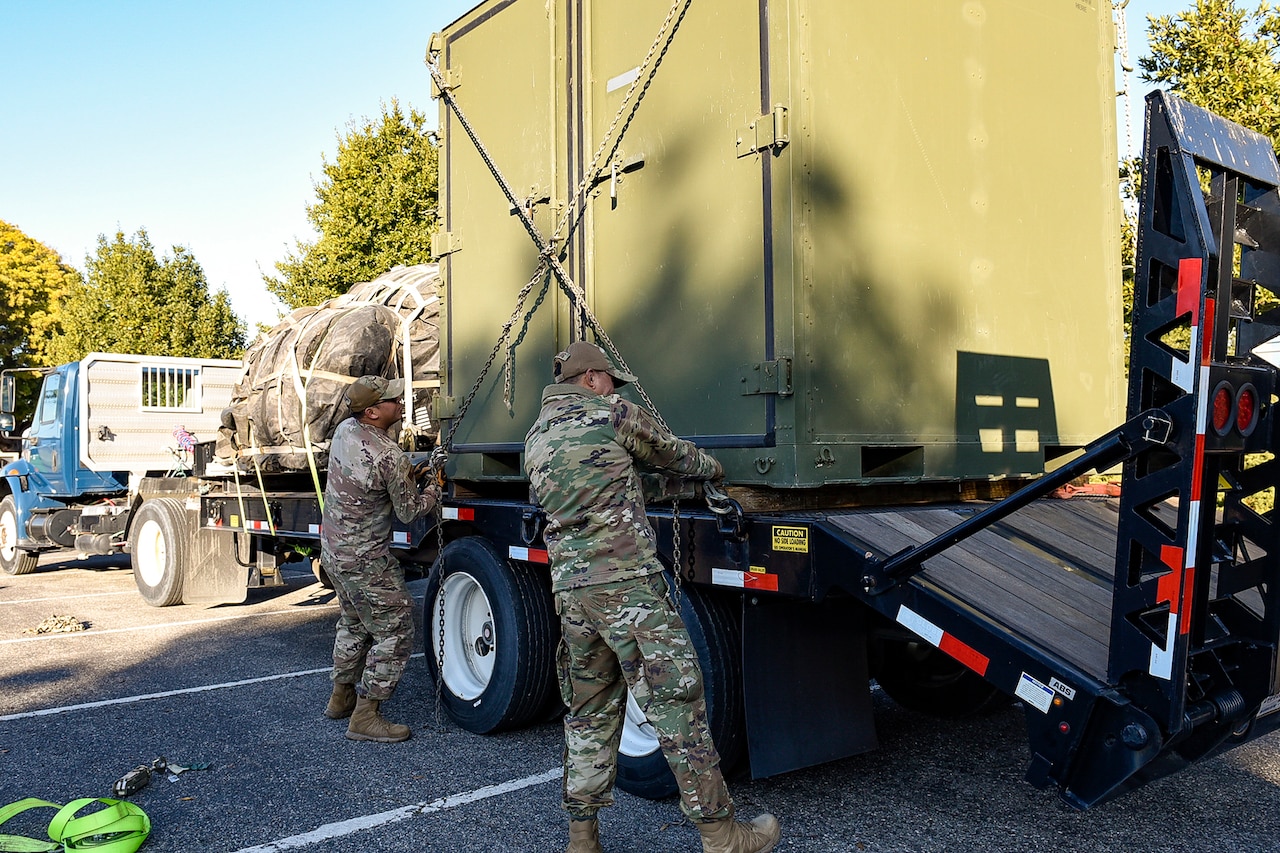 Airmen load a large cargo pallet onto the back of a truck during the day.