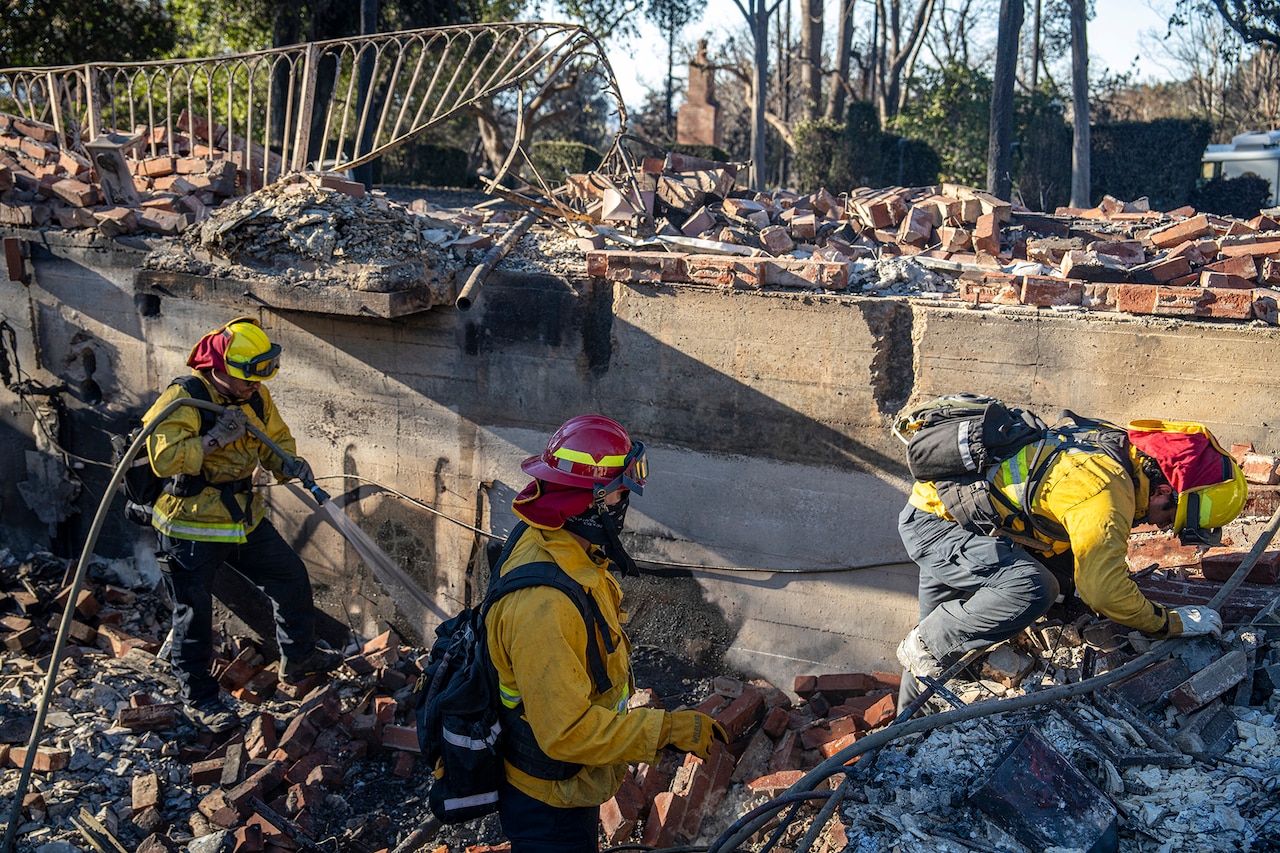 A group of firefighters work on clearing rubble from a burned building.
