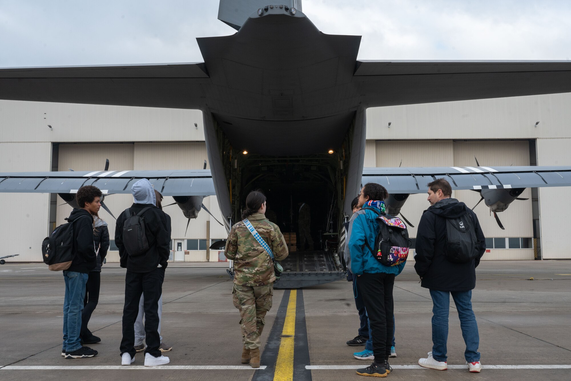 A woman stands near a C-130J with students