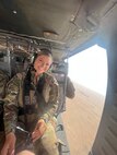 A woman in an Air Force uniform flies in a helicopter seat whith the door open.
