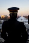 the U.S. Monument is in focus illuminated by the sunrise with silhouette of soldier looking at it in foreground slightly out of focus