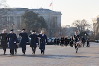 Service members salute while a drummer plays his instrument while marching off to the side