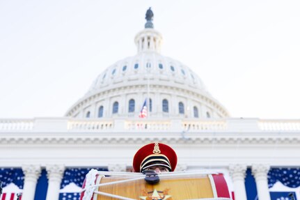 the top of a soldiers hat and eyes show behind his drum with the U.S. Capitol in the background.