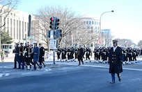 A joint service honor guard marches in a parade with Sailors behind them