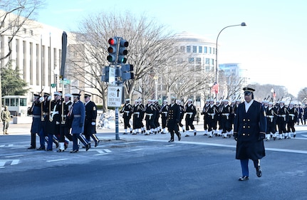 A joint service honor guard marches in a parade with Sailors behind them