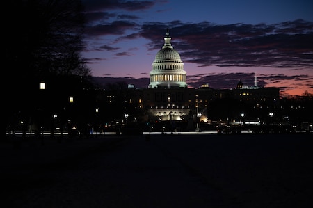 The U.S. Capitol is illuminated slightly as the sun rises behind it