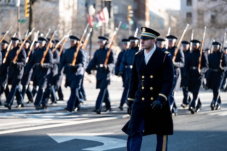 A soldier looking out into the distance with Airmen in background marching in formation