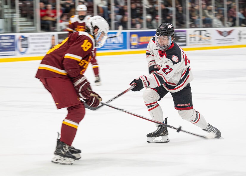 Reid Arnold (right), Minot State University Beavers defenseman, attempts a shot on goal past Michael Mulkerrin (left), Iowa State University Cyclones forward, during the MSU military appreciation hockey game at Maysa Arena, Minot, ND, Jan. 11, 2025. Arnold scored two of the Beaver’s 12 goals during the game. (U.S. Air Force photo by Senior Airman Kyle Wilson)