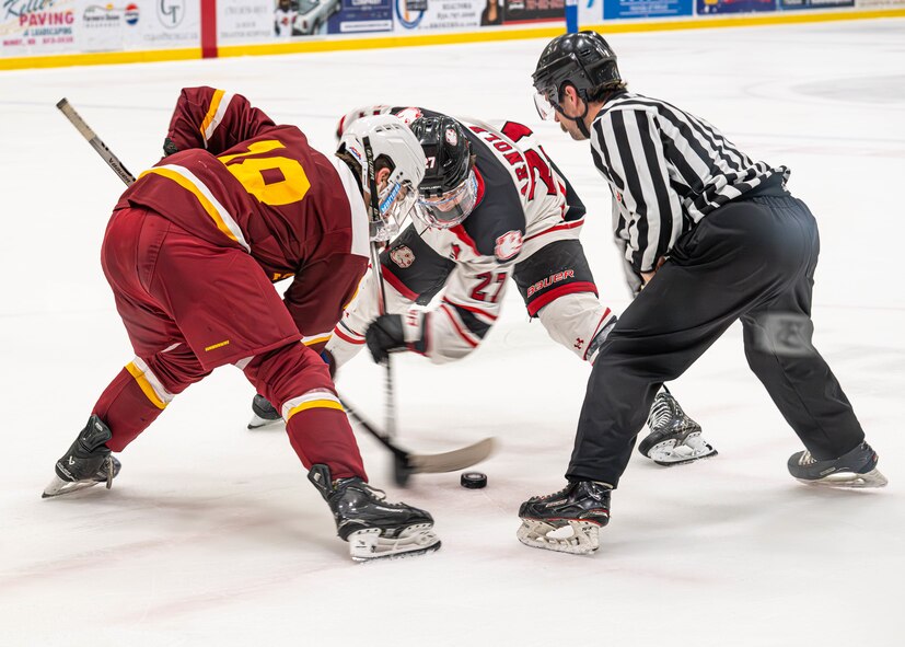 Michael Mulkerrin (left), Iowa State University Cyclones forward, and Reid Arnold (center), Minot State University Beavers defenseman, conduct a face-off during the Minot State University military appreciation hockey game at Maysa Arena, Minot, North Dakota, Jan. 11, 2025. A face-off is the method of restarting play during a hockey game after a penalty occurs or a goal is scored. (U.S. Air Force photo by Senior Airman Kyle Wilson)
