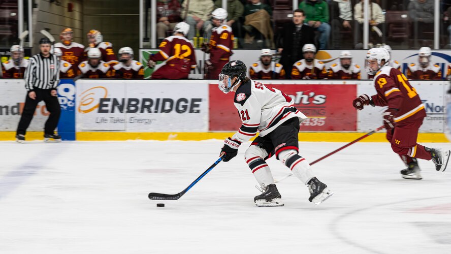 Slade Stanick (center), Minot State University Beavers forward, skates with the puck during the MSU military appreciation hockey game at Maysa Arena, Minot, North Dakota, Jan. 11, 2025. The Beavers controlled possession of the puck throughout most of the game. (U.S. Air Force photo by Senior Airman Kyle Wilson)