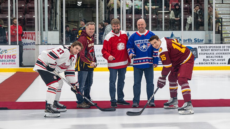 (From left) Reid Arnold, Minot State University Beavers forward, U.S. Air Force Col. Jimmy Schlabach, 91st Missile Wing commander, Dr. Steven Shirley, Minot State University president, U.S. Air Force Col. Benjamin Jensen, 5th Bomb Wing deputy commander, and Jacob Schuldt, Iowa State University Cyclones defenseman, participate in a ceremonial puck drop during the MSU military appreciation hockey game at Maysa Arena, Minot, North Dakota, Jan. 11, 2025. The ceremonial puck drop is a longstanding tradition in ice hockey, which involves a guest of honor dropping a puck to commemorate the beginning of the game. (U.S. Air Force photo by Senior Airman Kyle Wilson)