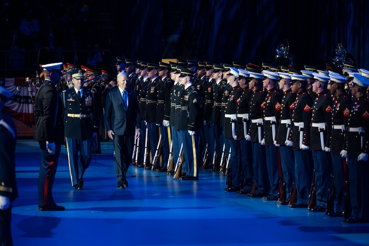 Two men walk together past dozens of uniformed service members.