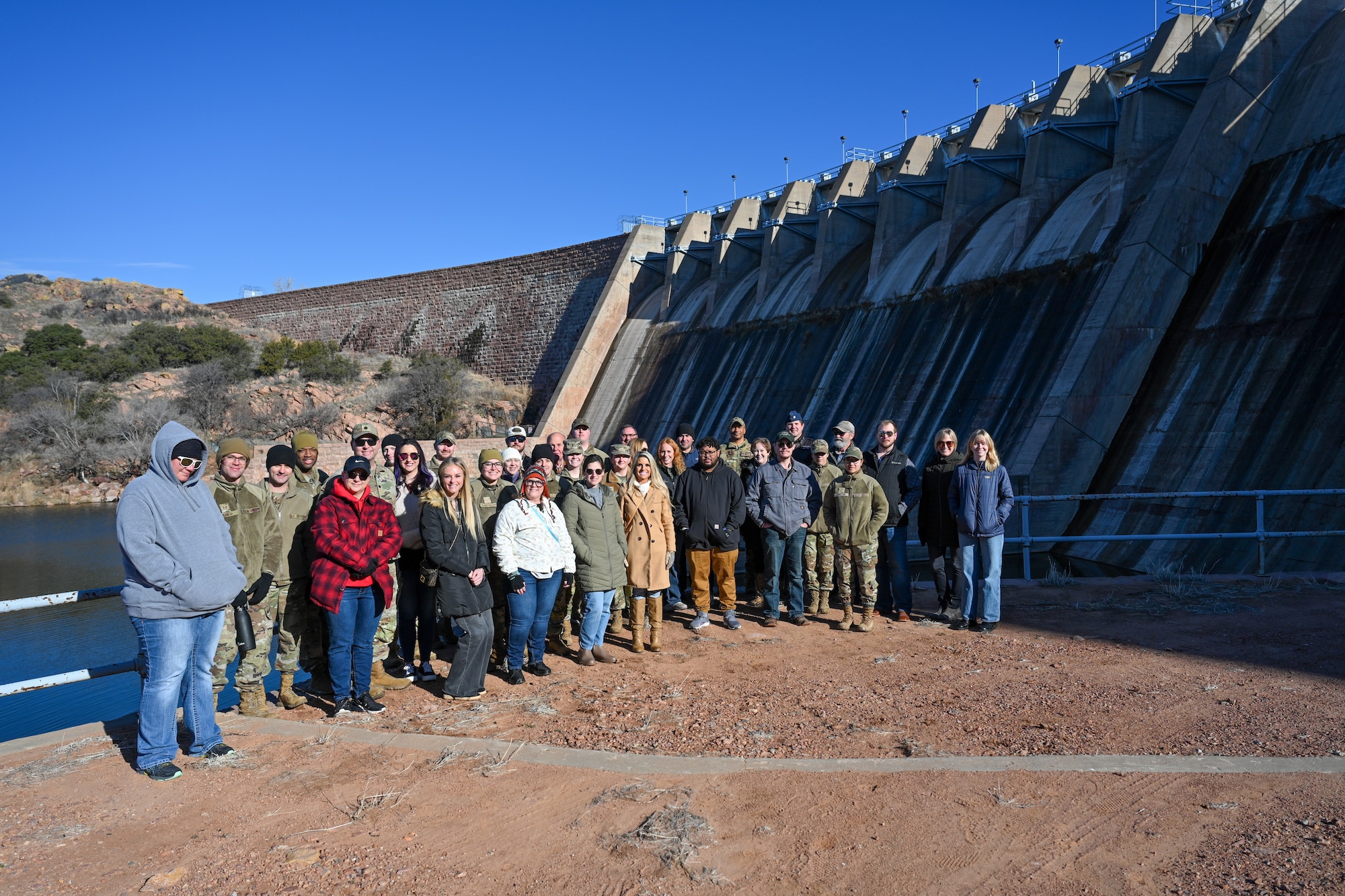 Airmen from the 97th Air Mobility Wing and members of the local community gather for a group photo in front of the dam at Lake Altus-Lugert, Oklahoma, Jan. 15, 2025. The group took a tour of the dam and learned about its history. (U.S. Air Force Photo by Airman 1st Class Jonah Bliss)