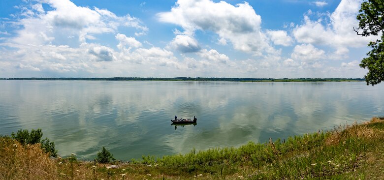 A body of water with a cloudy sky in the background and brown vegetation in the foreground.