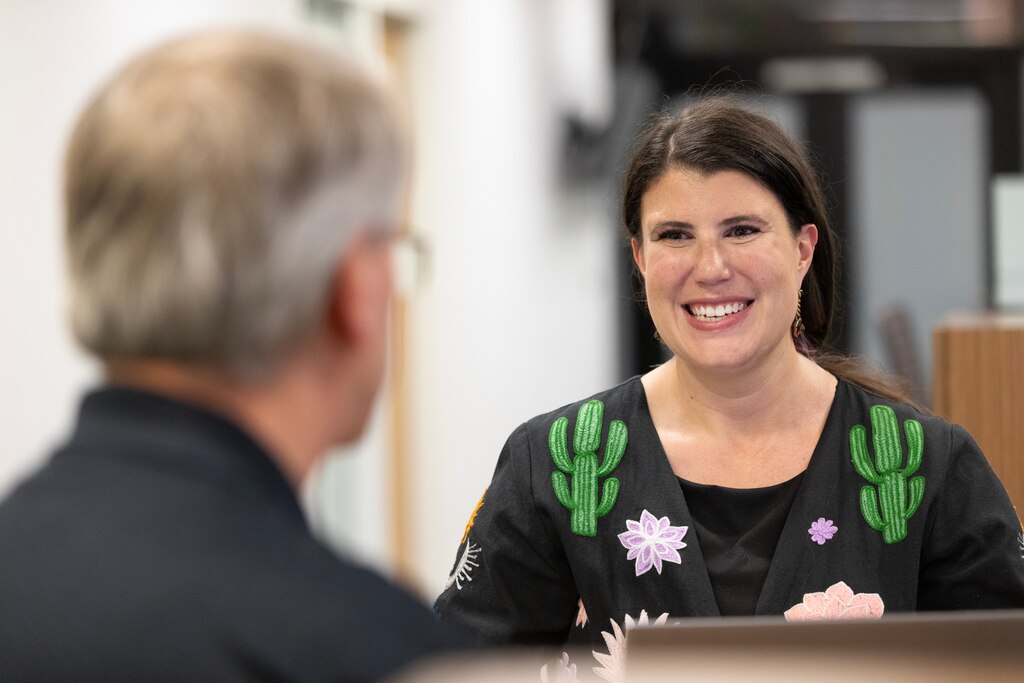 A man in a black shirt has his back turned and a woman in a black shirt with green cacti on the shoulders looks at him and smiles.