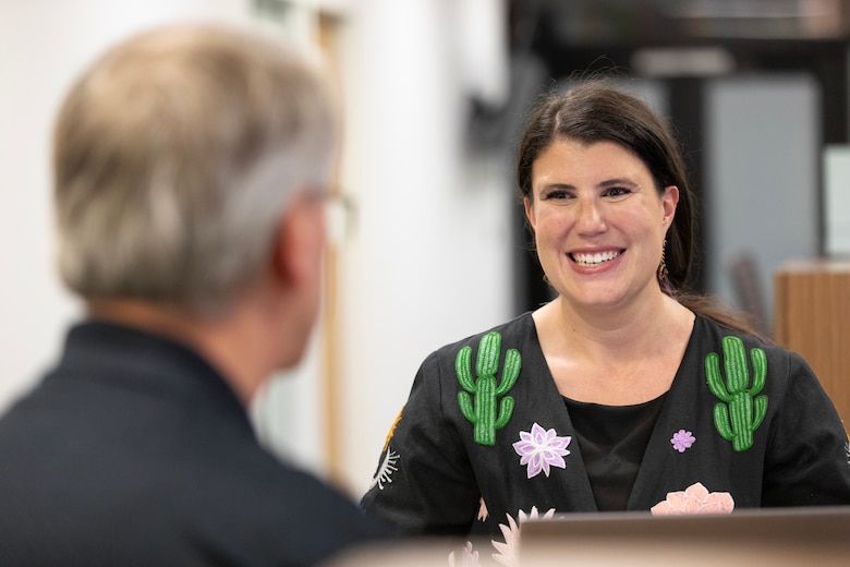 A man in a black shirt has his back turned and a woman in a black shirt with green cacti on the shoulders looks at him and smiles.