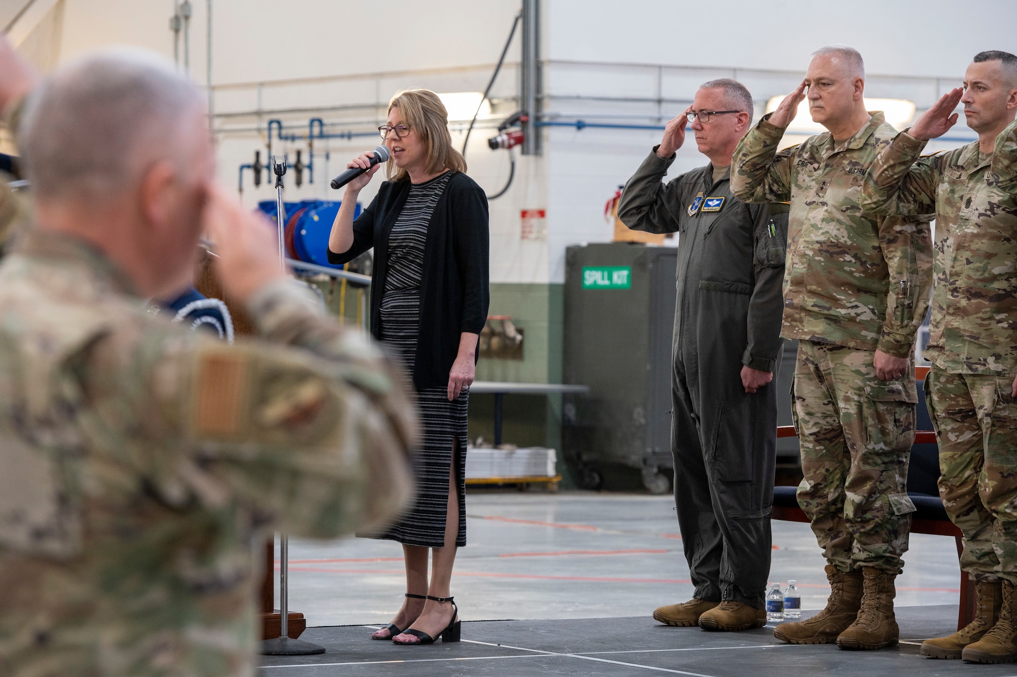 a women stands on stage and sings into a microphone as other around her salute