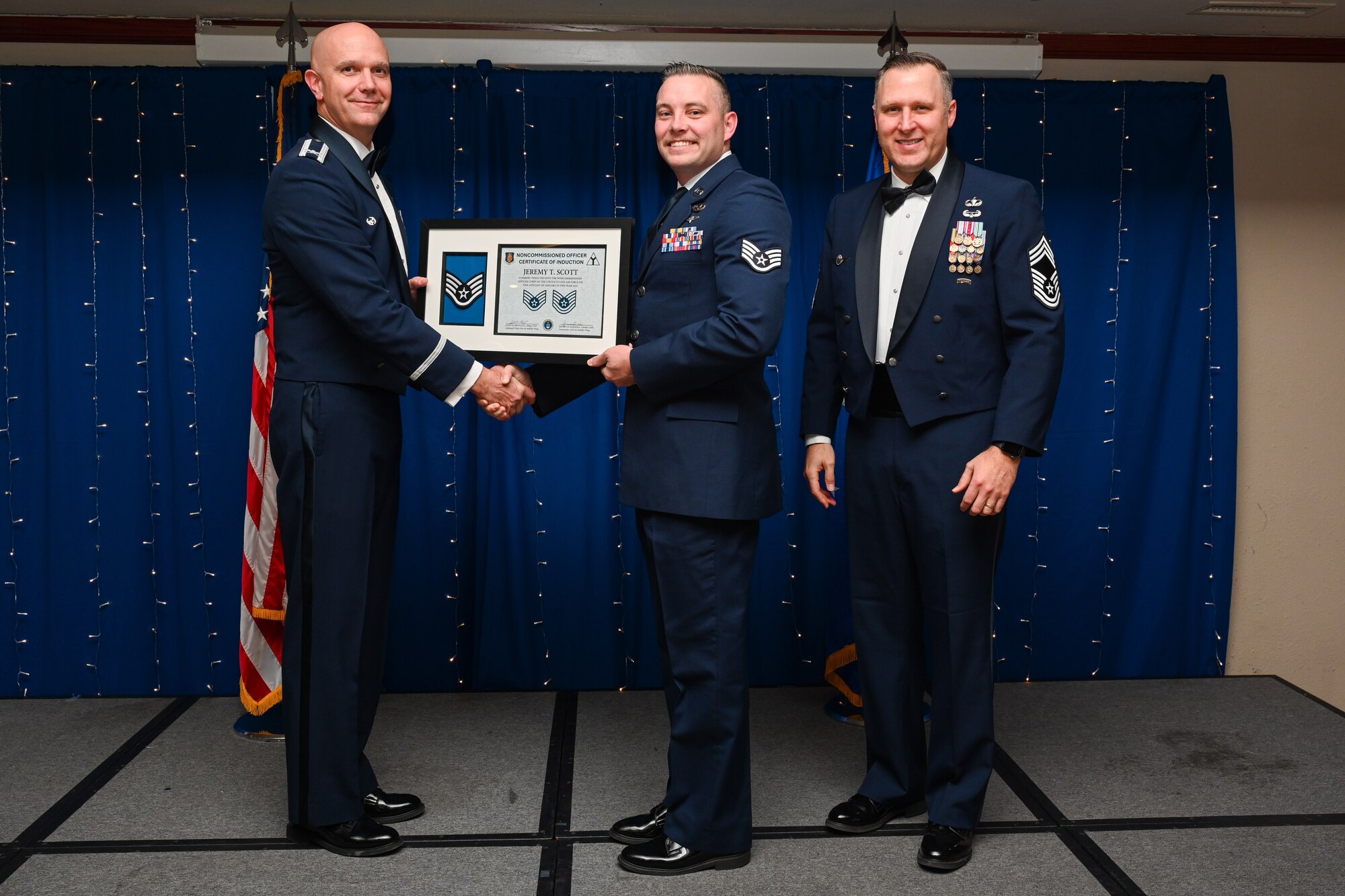 U.S. Air Force Staff Sgt. Jeremy Scott, 97th Logistics Readiness Squadron noncommissioned officer in charge of fleet services, center, receives a noncommissioned officer (NCO) certificate of induction in Club Altus at Altus Air Force Base, Oklahoma, Jan. 16, 2025. Altus Air Force Base held its first ever NCO induction ceremony to celebrate Airmen entering the noncommissioned officer corps. (U.S. Air Force Photo by Airman 1st Class Jonah Bliss)