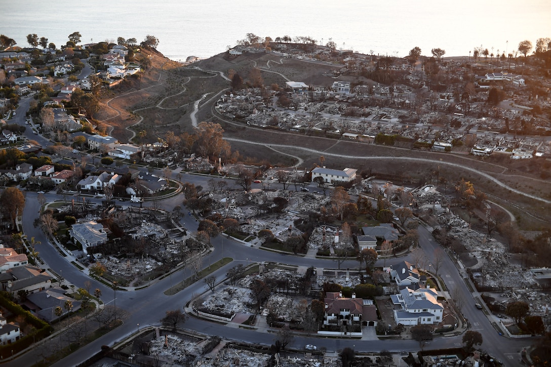 An aerial view of a hilly neighborhood with numerous demolished homes interspersed with homes still standing.