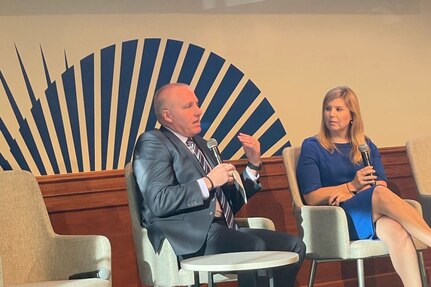 A man and a woman sit and address an off-camera audience.