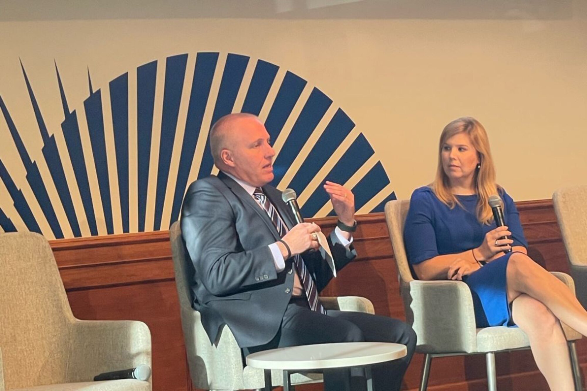 A man and a woman sit and address an off-camera audience.
