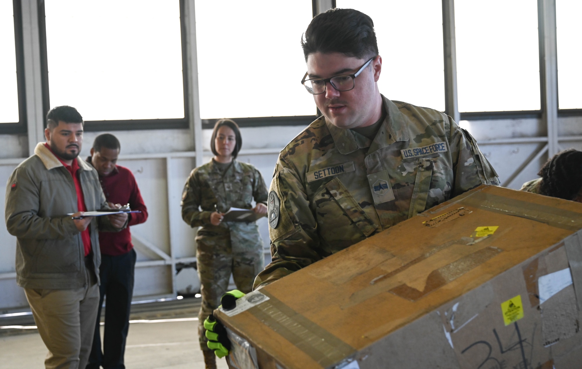 U.S. Space Force Spc. 4 Blake Settoon, 62nd Cyberspace Squadron defensive cyber operator, carries a box during the space logistics challenge at Peterson Space Force Base, Colorado, Jan. 25, 2025. Settoon was the only member to participate that had zero experience in loading/unloading containers for this event, helping build the baseline that was used to compare the instructions given by artificial intelligence. (U.S. Space Force photo by Staff Sgt. Jaime Sanchez)