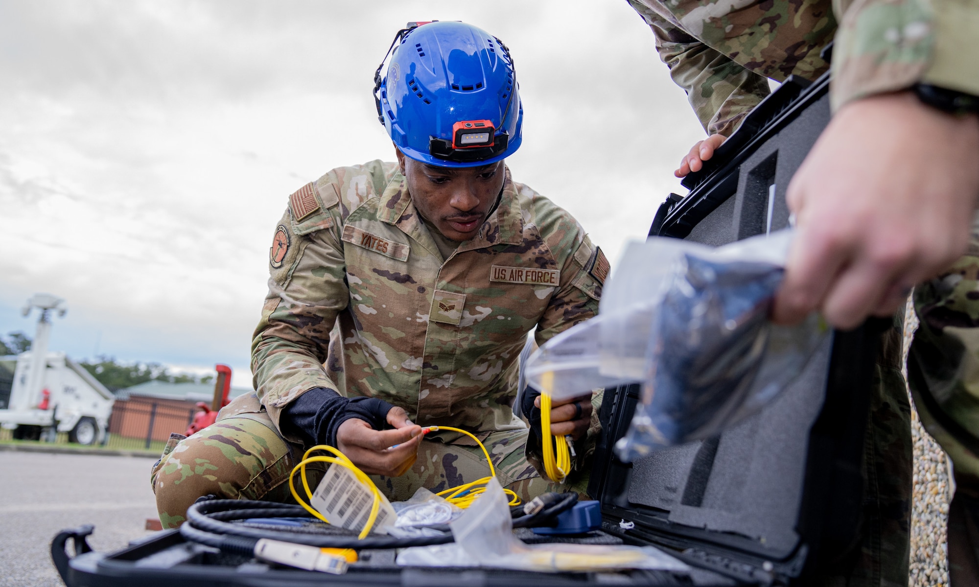 A serviceman in an operational camouflage pattern uniform looks inside a box containing wires and cords.