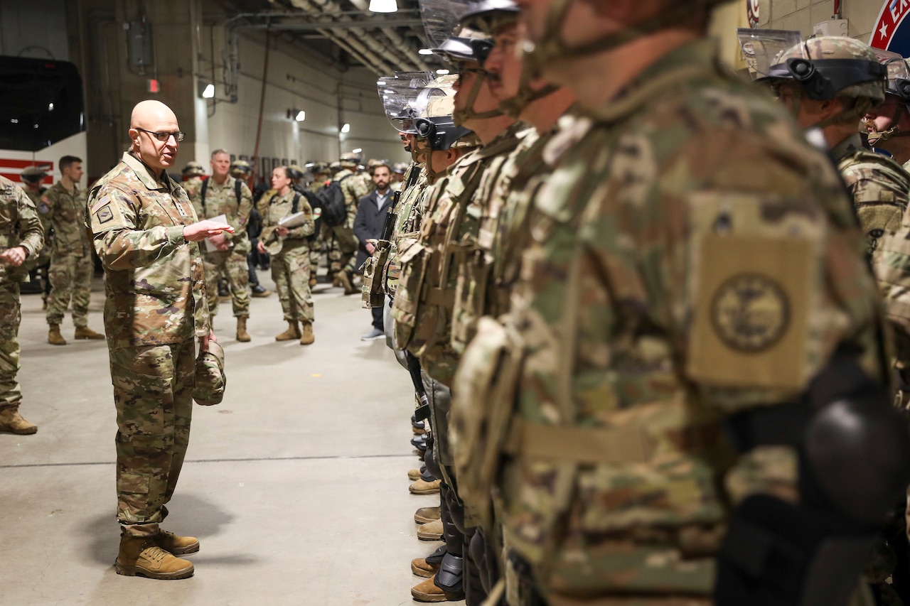 An Army general speaks to a group of guardsmen inside a large room.