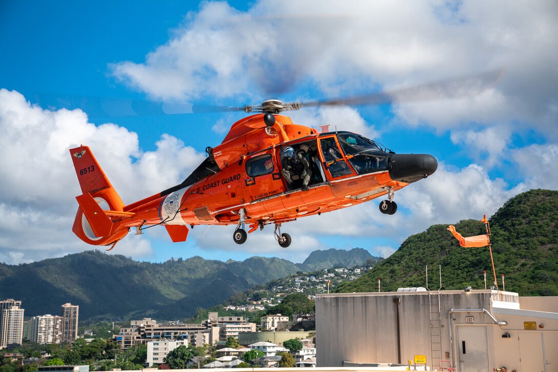 A Coast Guard MH-65 Dolphin helicopter crew assigned to Air Station Barbers Point approaches the landing pad at Queen's Medical Center for flight training in Honolulu, Hawaii, Dec. 14, 2024. Air Station Barbers Point air crews routinely conduct touch-and-go flight training at various locations to enhance area familiarization to maintain readiness for search and rescue cases. (U.S. Coast Guard photo by Petty Officer 2nd Class Tyler Robertson)