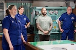 Coast Guard military members and a civilian employee are standing and shown smiling.