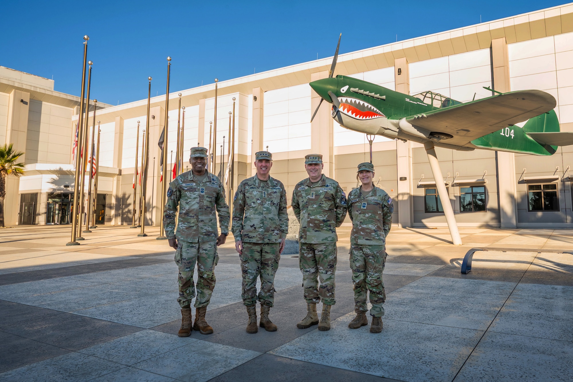 A group of four military leaders stand together for a group photo outside a building.