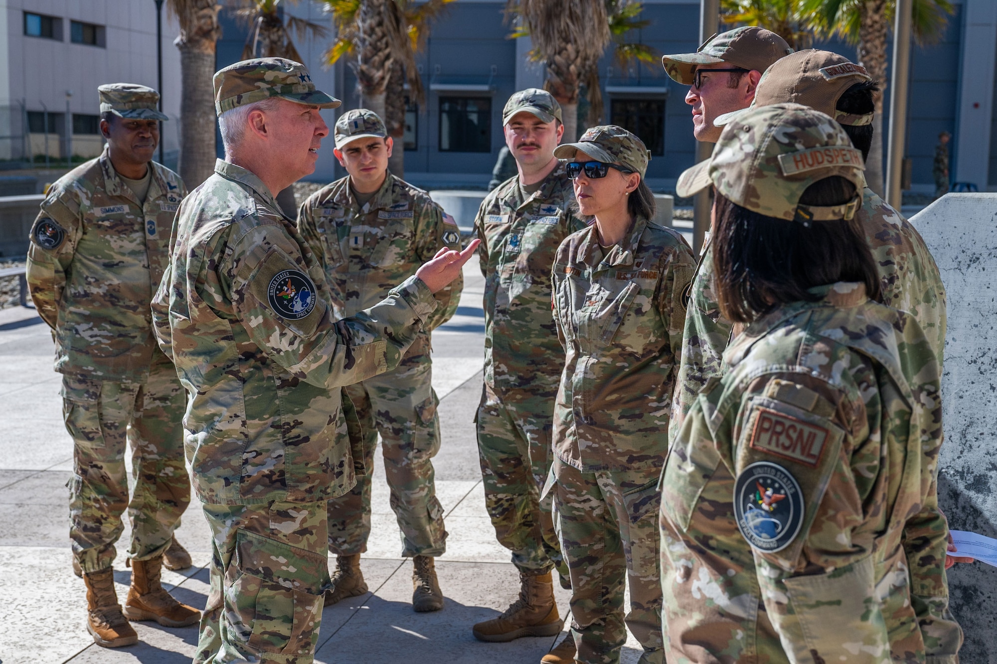 A group of military members stand outside in a courtyard talking with one another.