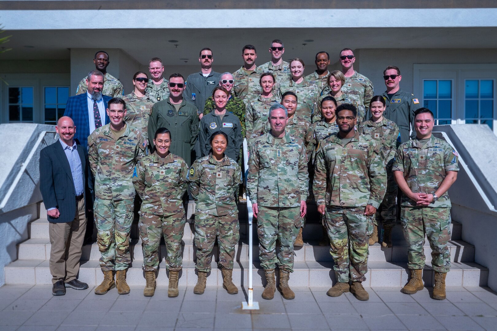 A group of military members stand together on steps for a group photo.