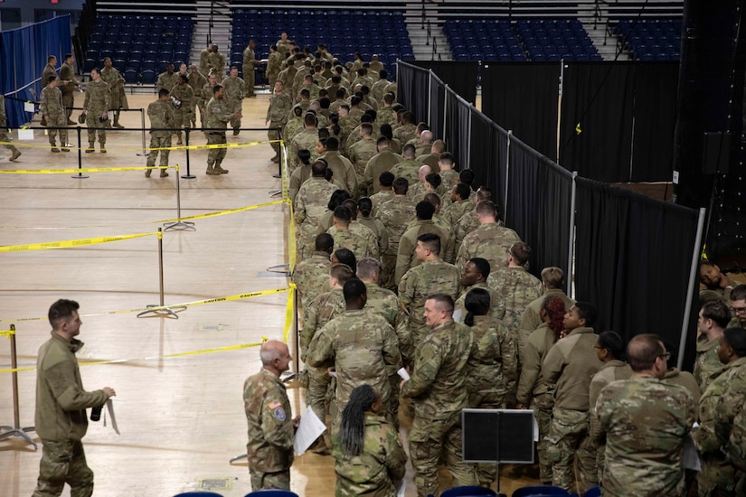 A group of soldiers line up indoors at a gymnasium.