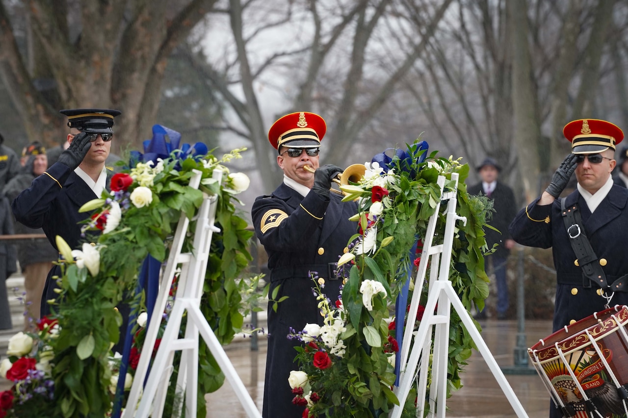 A group of soldiers performs in front of wreaths outdoors during a cloudy day.