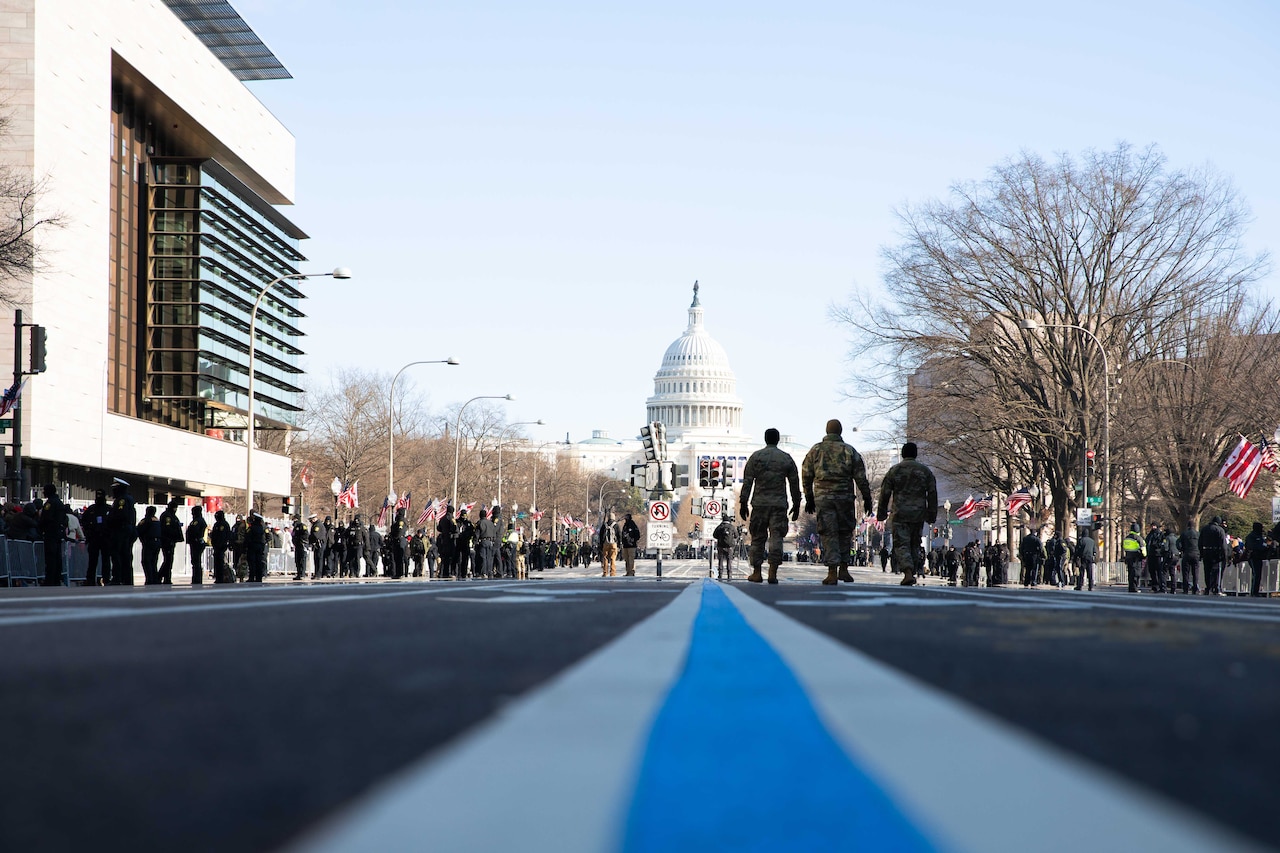 Soldiers patrol down a road with the Capital building in the distance during a clear day.