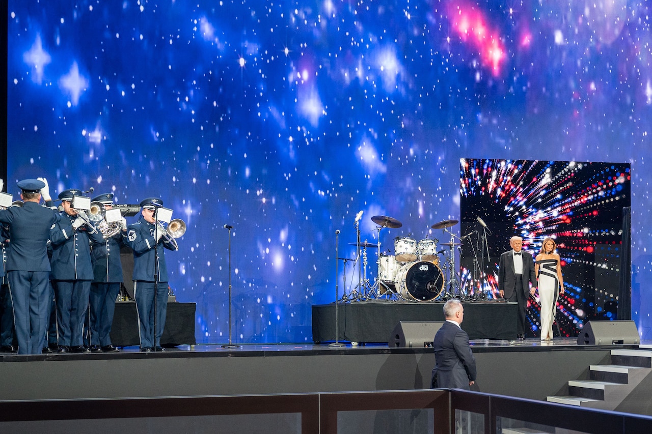 A couple in elegant attire enters the stage from a door on the right while a military band plays on stage on the left.
