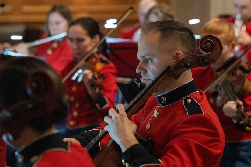 A Marine plays an instrument while in a group of other Marines playing.