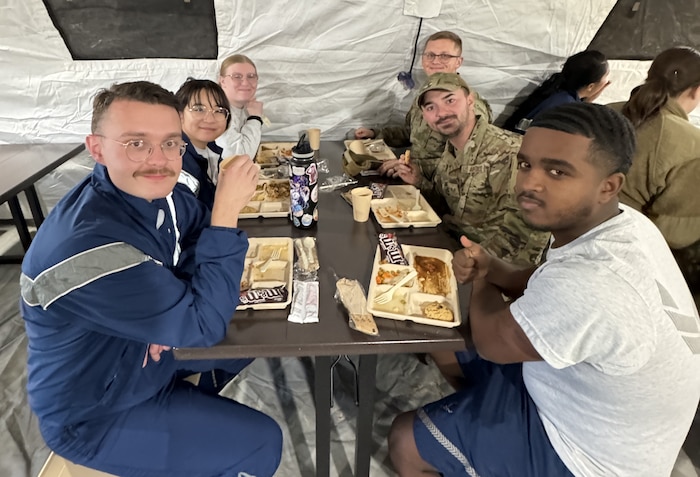 Six Airmen sitting at a table in a tent looking at the camera with their trays in front of them.