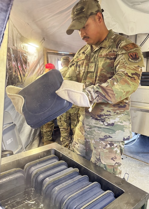 Airmen holds a gray square UGT while wearing heat protective gloves with the equipment holding eight other UGTs in the foreground.